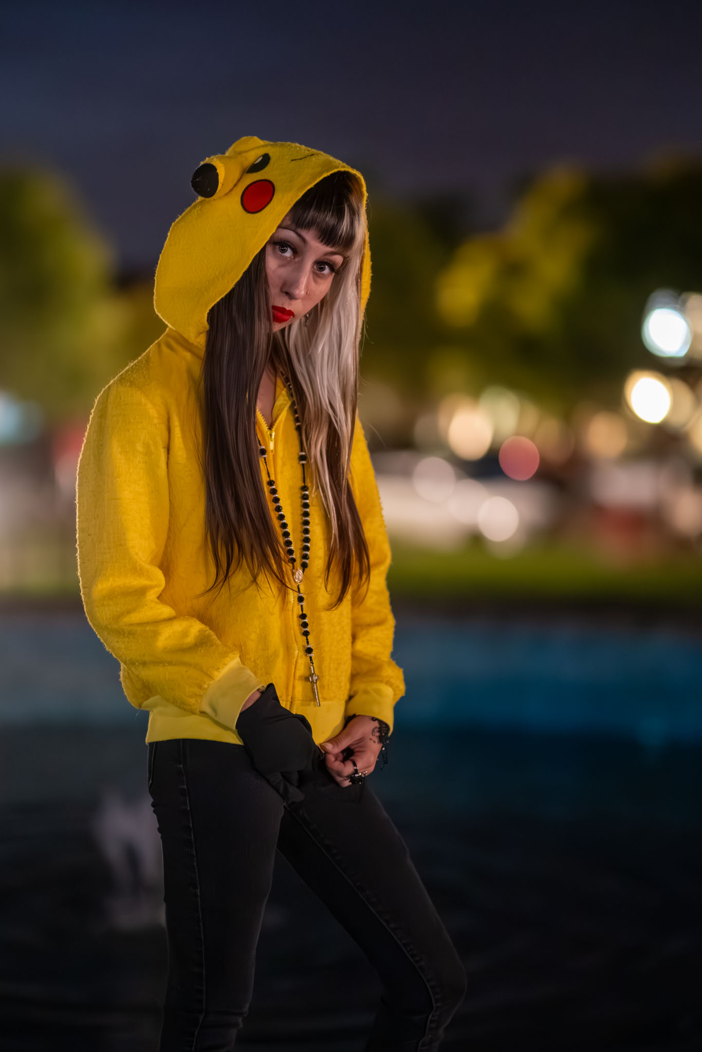 A woman peers out from beneath a yellow Pikachu-eared hoodie in dusk light.
